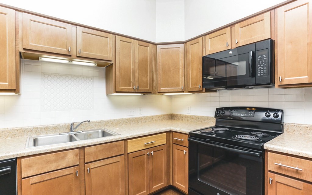 a kitchen with wooden cabinets and a black stove and a microwave at East Meadows apartments in San Antonio, TX