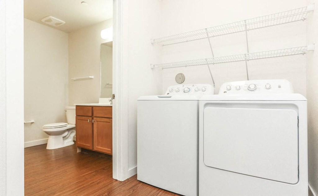 a white washer and dryer in a room with a toilet and a bathroom at East Meadows apartments in San Antonio, TX
