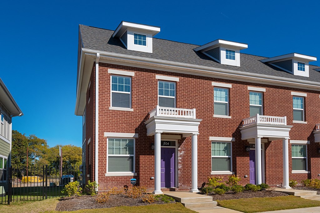a red brick house with purple doors and a black fence