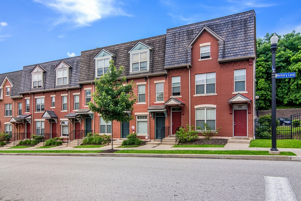 A row of red brick townhouses with green doors and windows.