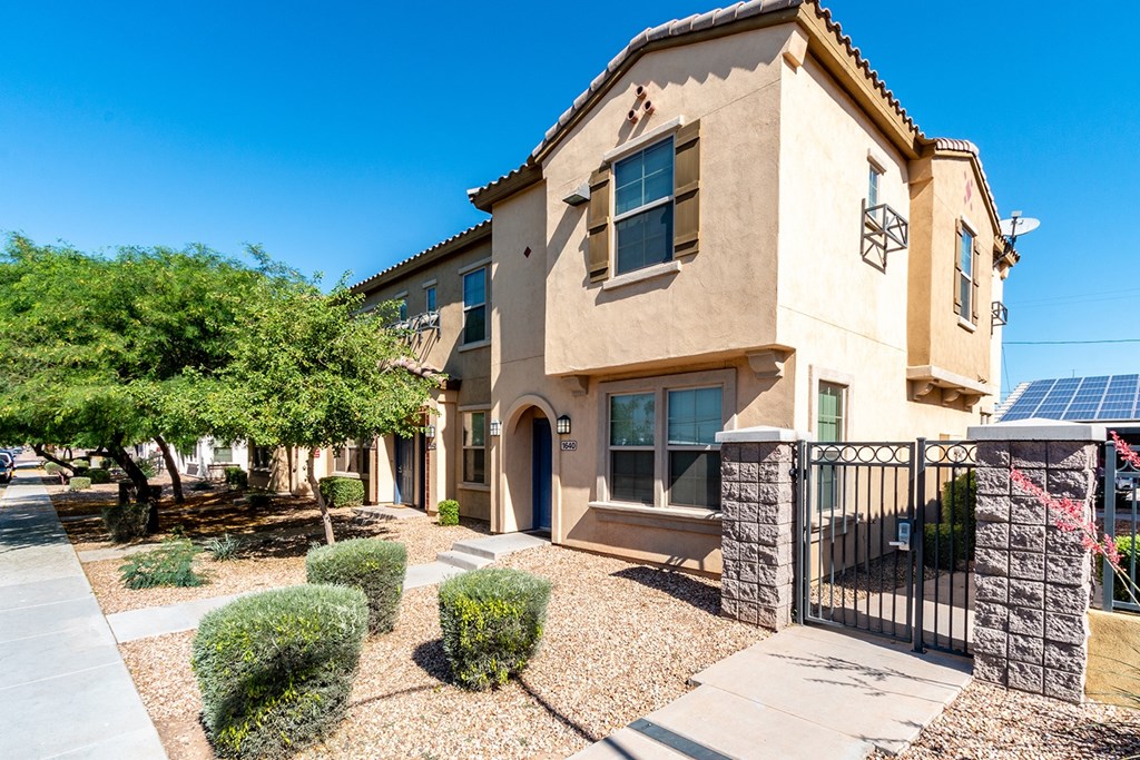 A beige house with a black gate and a small garden in front.