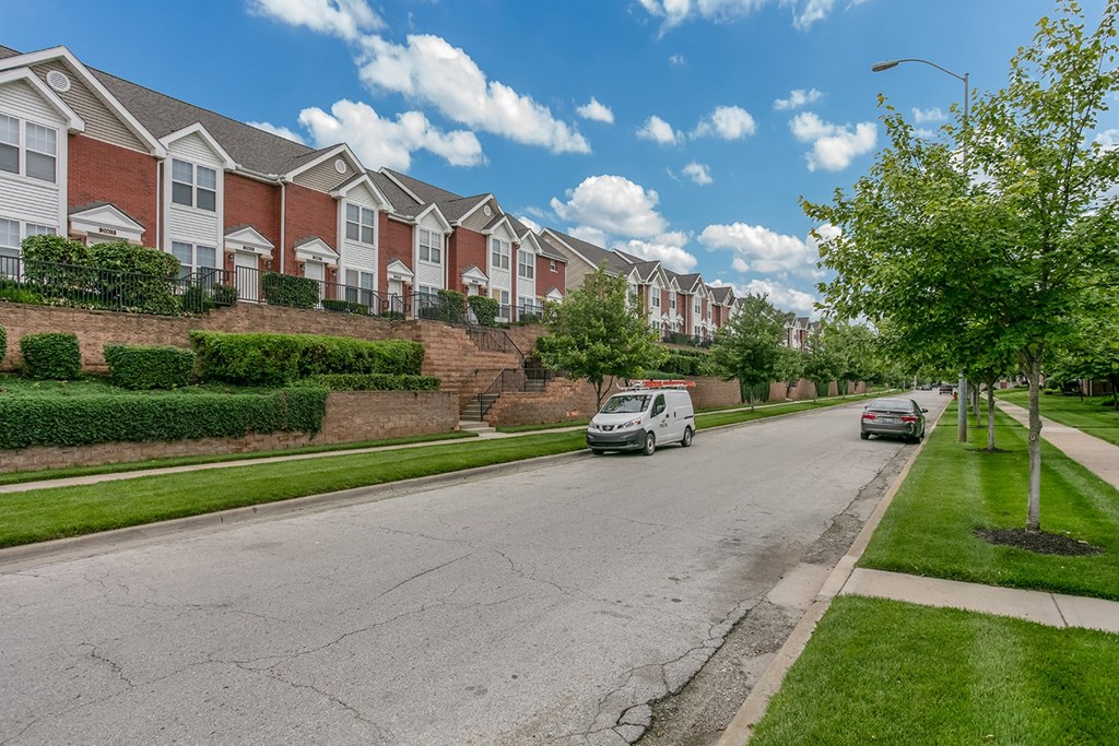 A street view of a residential area with houses on one side and cars parked on the other.