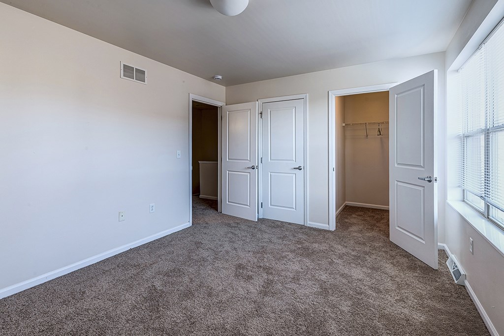A room with white walls and a carpeted floor with a ceiling fan.