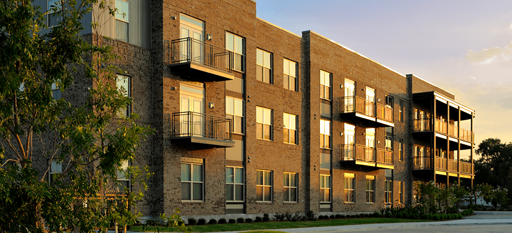 a brick apartment building with balconies and a sunset in the background