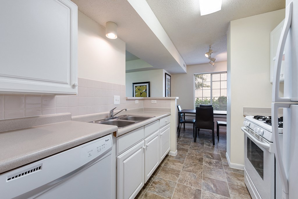 an open kitchen with white appliances and counters and a dining room with a window