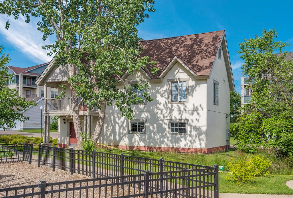 a white house with a fence and a tree in front of it
