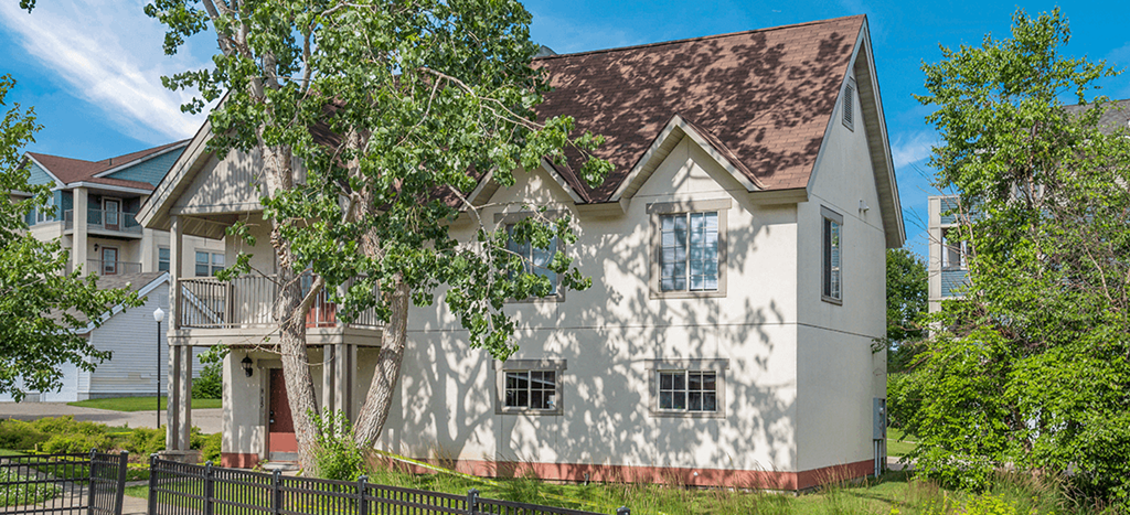 a white carriage house with a tree in front at Heritage Park Apartments