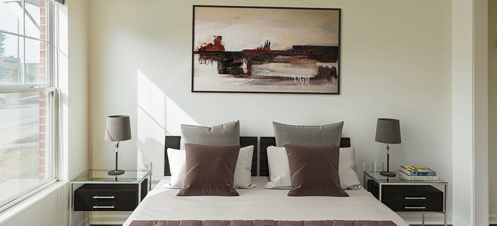 a bedroom with a bed and two side tables, artwork hangs on the wall above the headboard