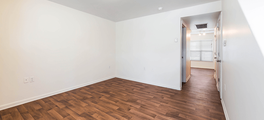 an empty bedroom with wood flooring and white walls