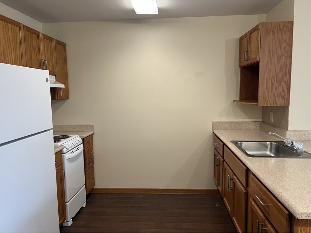 A kitchen with a white fridge, wooden cabinets, and a sink.