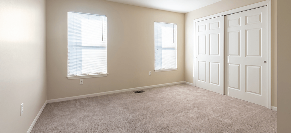 an empty bedroom with two windows and a closet door