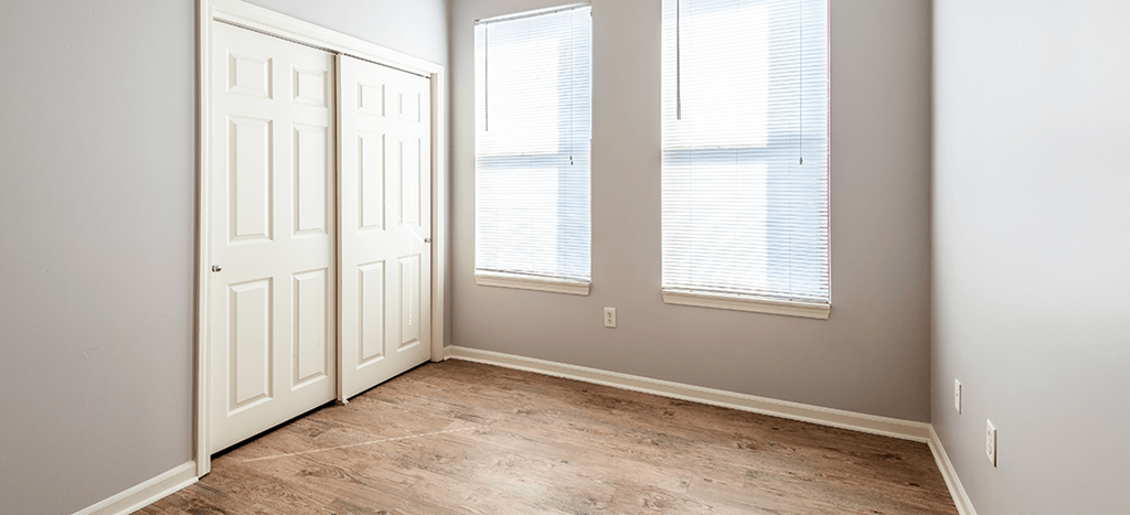 an empty bedroom with a closet door and two windows