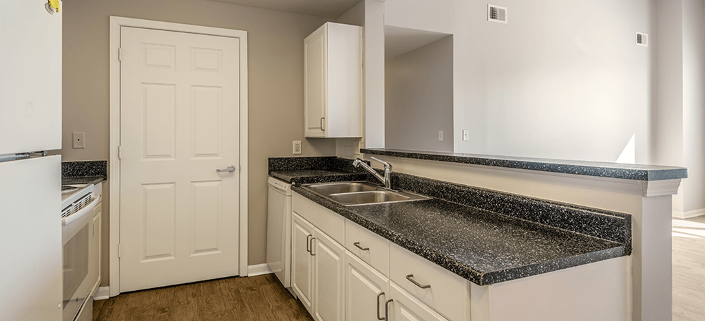 an empty kitchen with gray counter tops and white cabinets