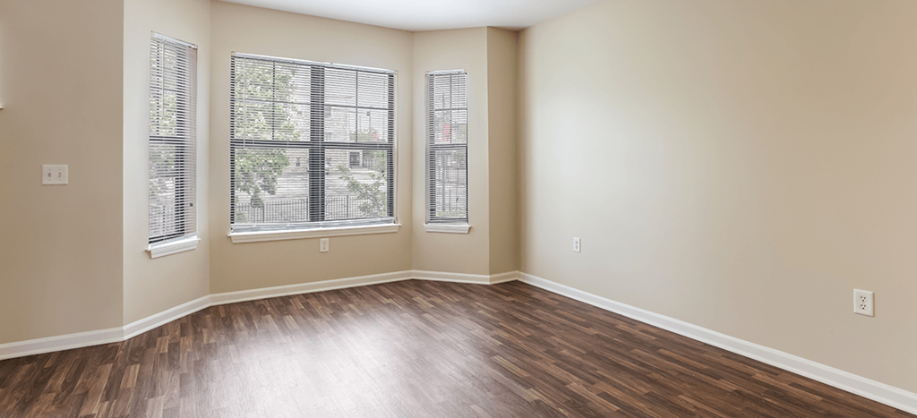 an empty living room with wood flooring and three windows
