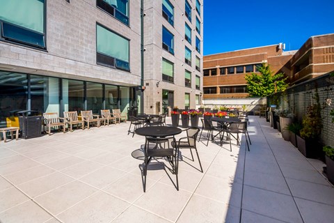 A patio with tables and chairs is surrounded by buildings.