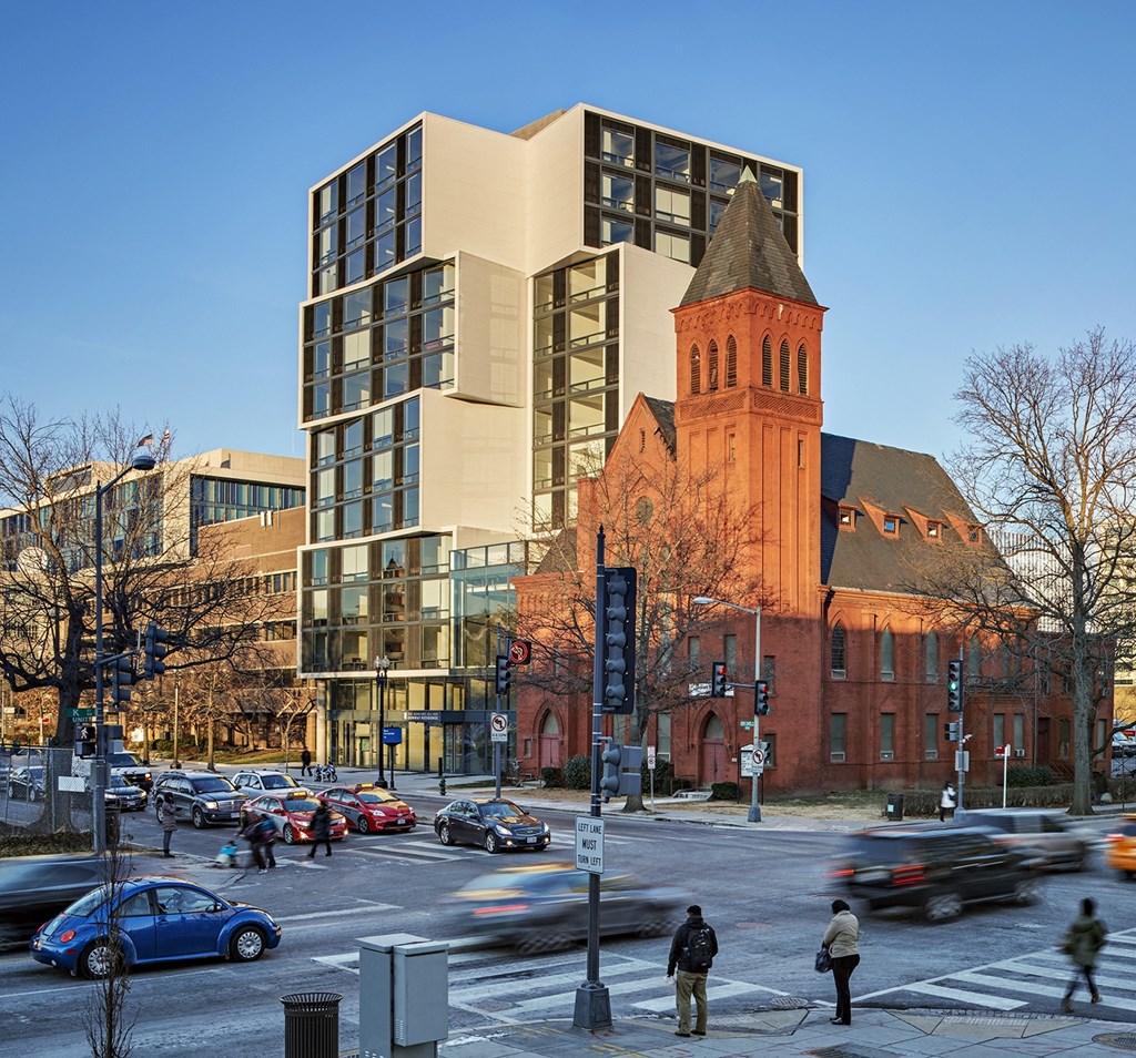 A busy street with cars and pedestrians in front of a church and a modern building.