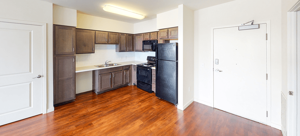 an empty kitchen with wood flooring and a black refrigerator