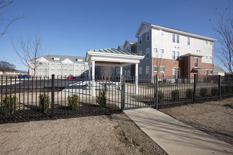 A white building with a green roof is behind a black fence.