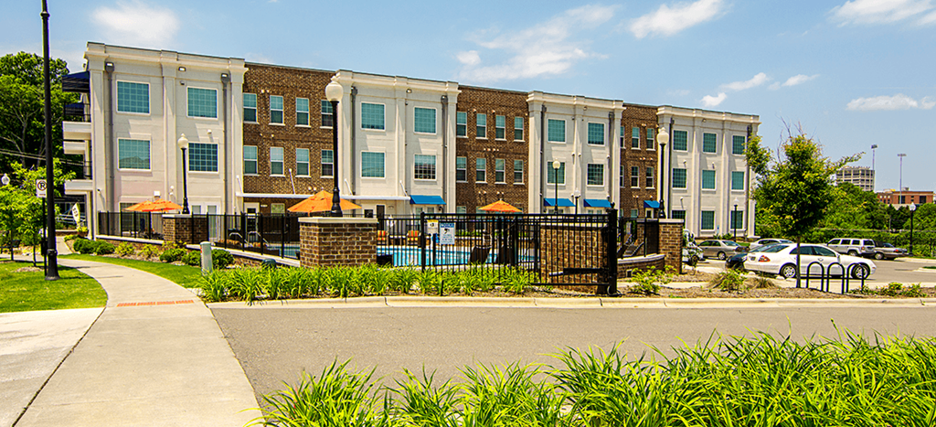 a row of brick apartment buildings next to a pool area with a street in front