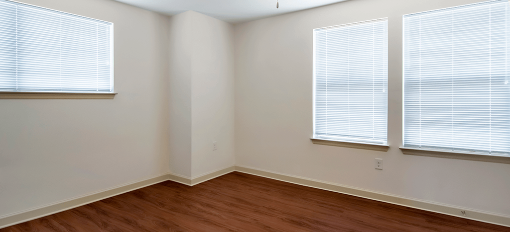 an empty bedroom with wood floors and three windows