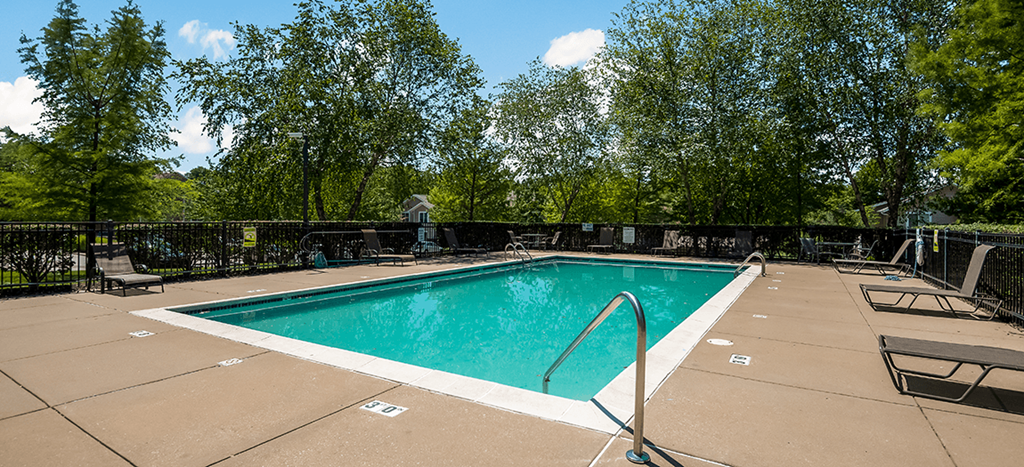 a swimming pool with chairs and trees in the background at Longfellow Heights Apartments