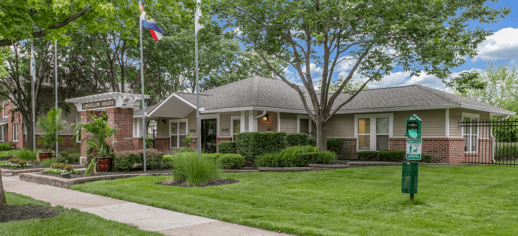 the front of an apartment leasing office at Longfellow Heights with a lawn and a flag