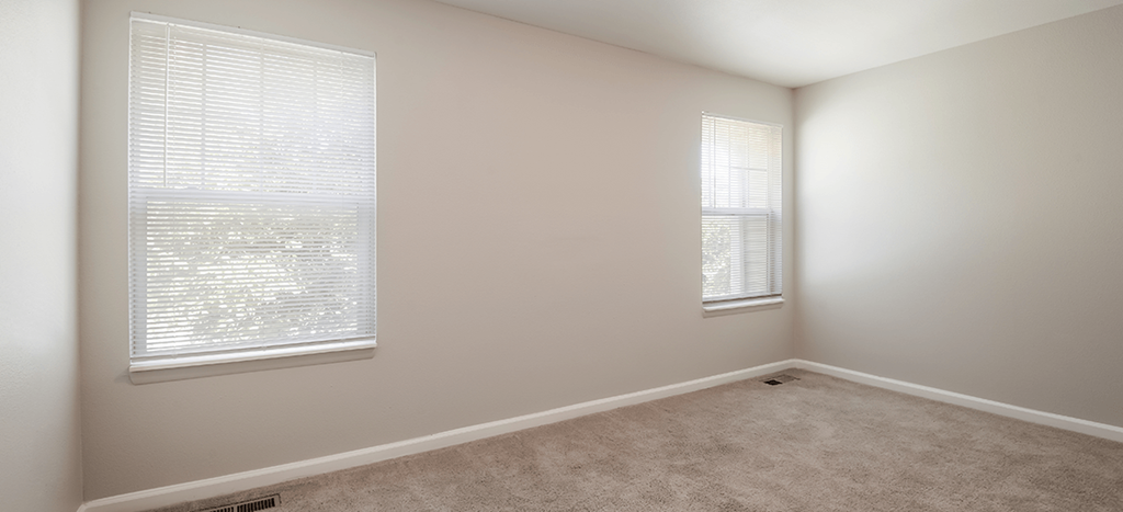 an empty bedroom with two windows and a carpet