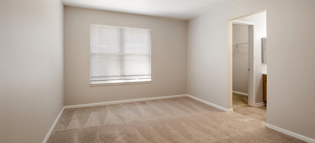 an empty bedroom with a window and a doorway to a bathroom and closet