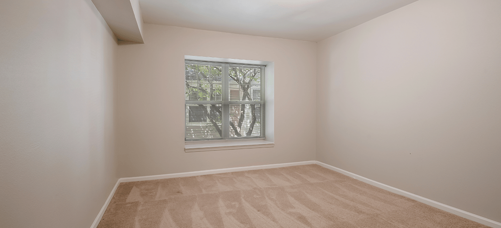 an empty bedroom with a window in the corner at Longfellow Heights apartments