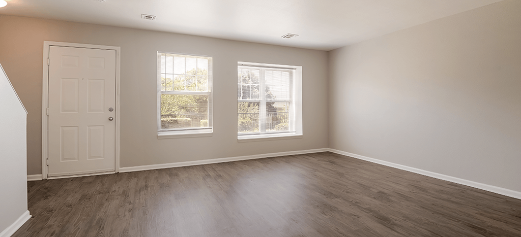 an empty living room with a door and two windows and a staircase at Longfellow Heights Apartments