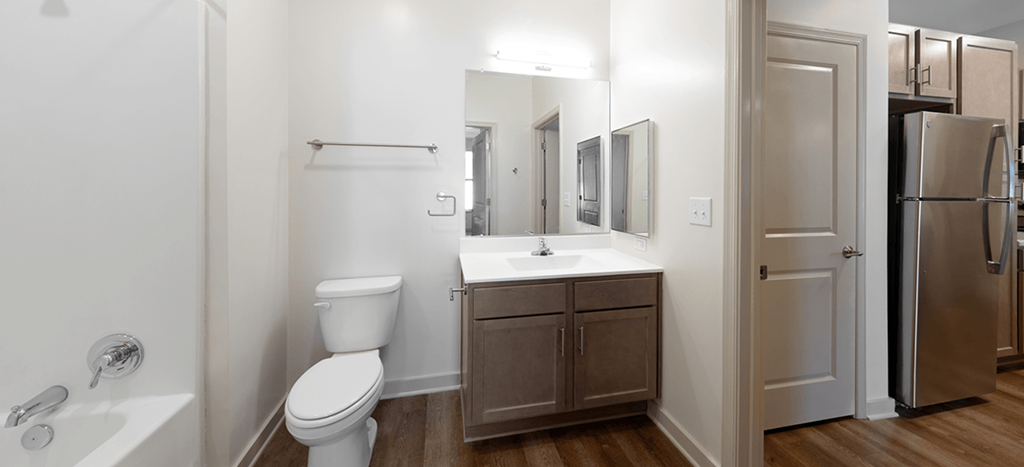 a bathroom with a toilet sink and mirror with a doorway to a kitchen