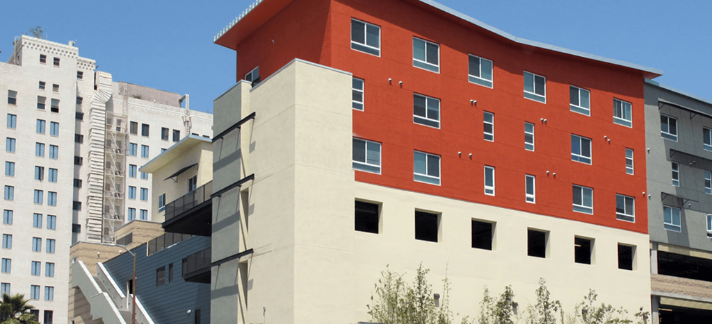 a large red apartment building in a city with other buildings