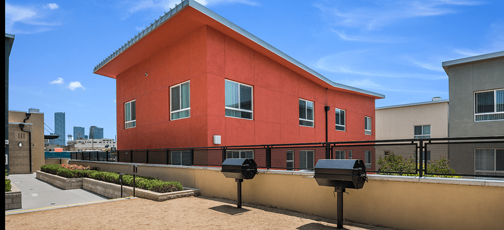 the back of a red apartment building with a BBQ area with two grills at MacArthur Park Apartments