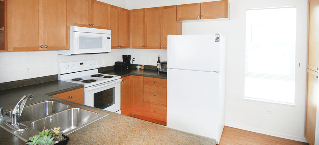 a kitchen at MacArthur Park Apartments with wooden cabinets and white appliances and a sink