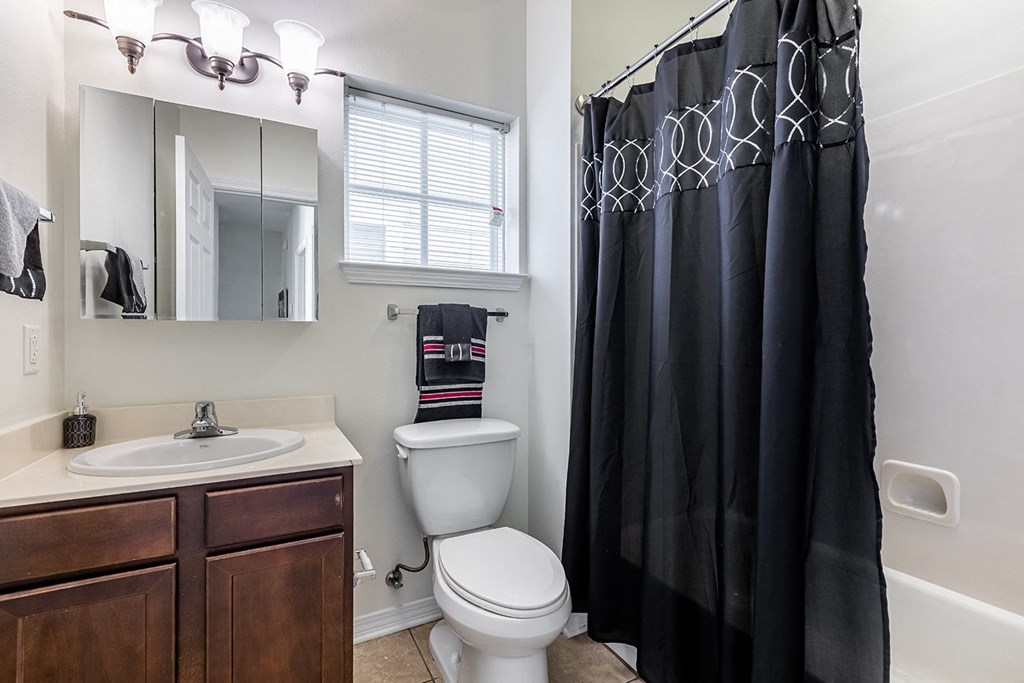 an updated bathroom with a black shower curtain and a toilet at Marrero Commons Apartments & Townhomes