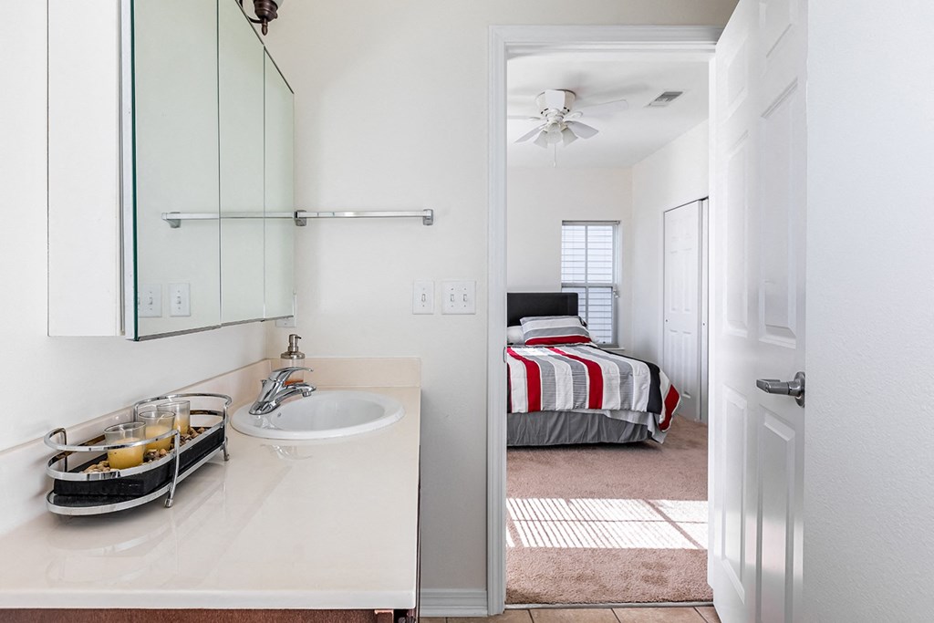 a bathroom with a sink and a mirror and a bedroom with a bed at Marrero Commons Apartments & Townhomes