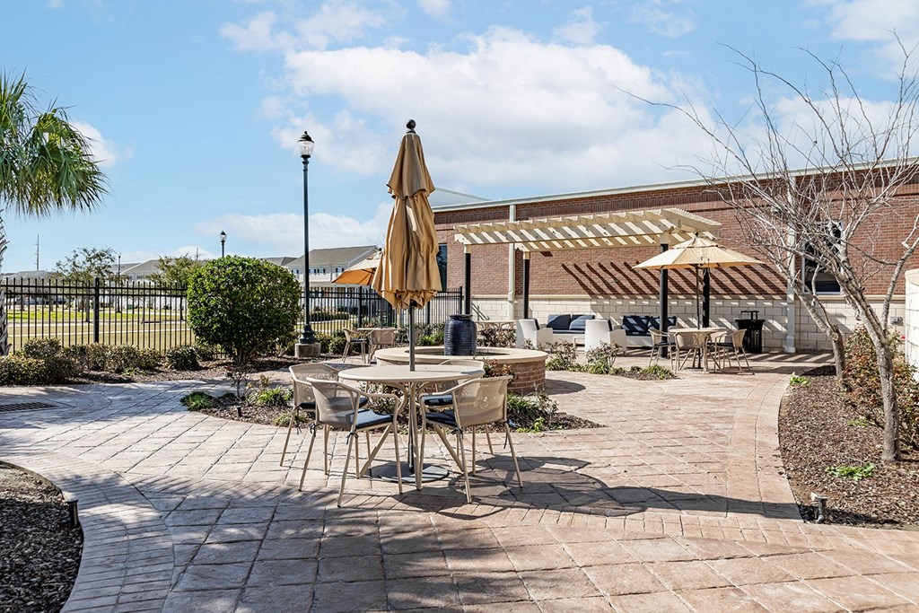 a patio with tables and umbrellas in front of a building at Marrero Commons Apartments & Townhomes