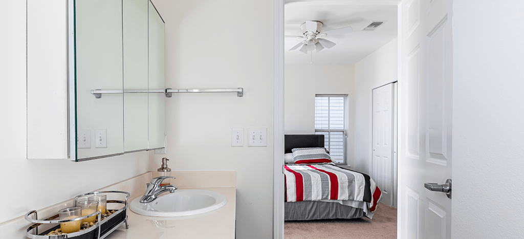 a bathroom with a sink and a mirror and a bedroom with a bed