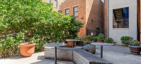 a patio with tables and benches in front of a brick building