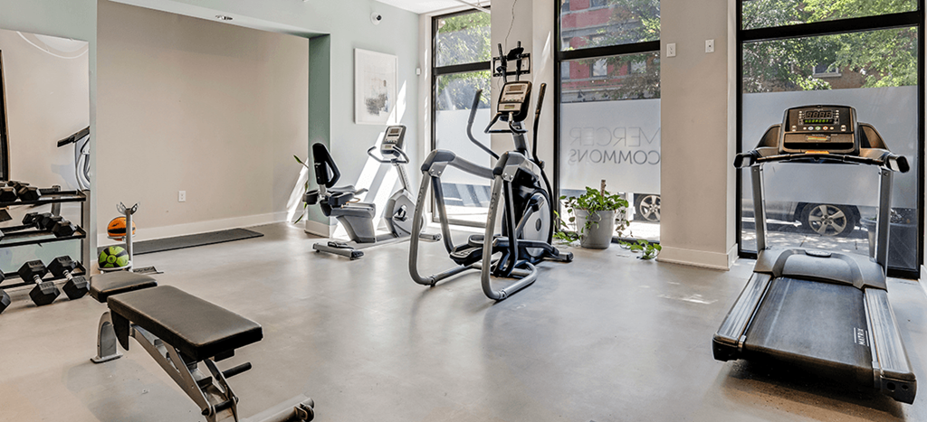 a gym with cardio equipment and a large window at Mercer Commons Apartments
