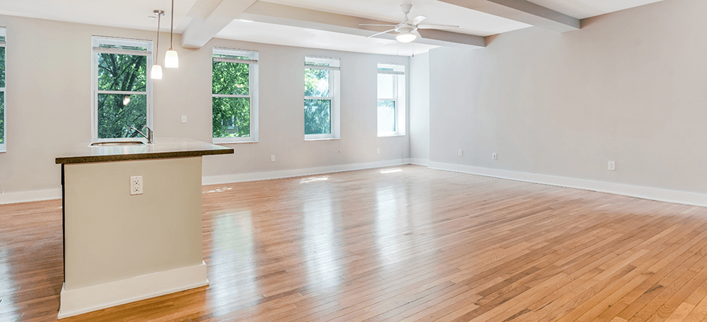 an empty living room with a kitchen and wood floors at Mercer Commons Apartments