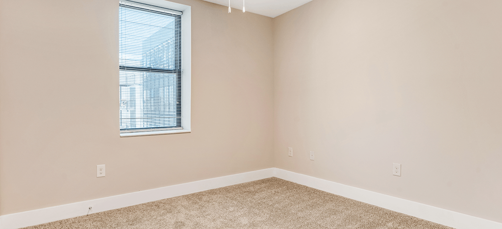 an empty bedroom with a window and carpeting at Mercer Commons Apartments