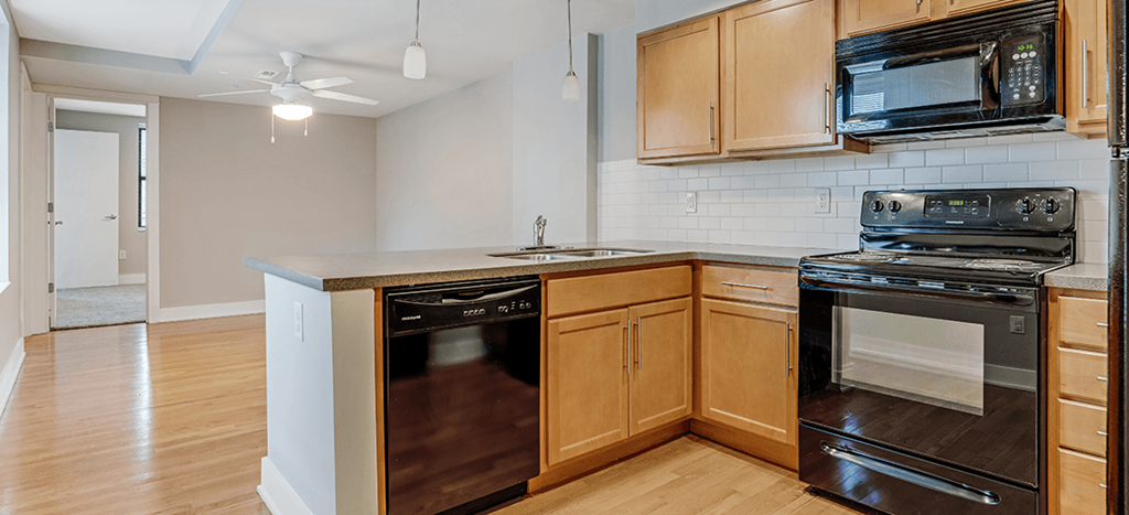 an empty kitchen with wooden cabinets and a stove and a microwave at Mercer Commons Apartments