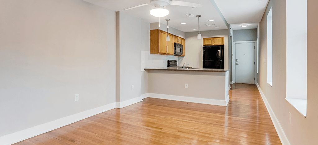 an empty living room with wood flooring and a kitchen at Mercer Commons Apartments