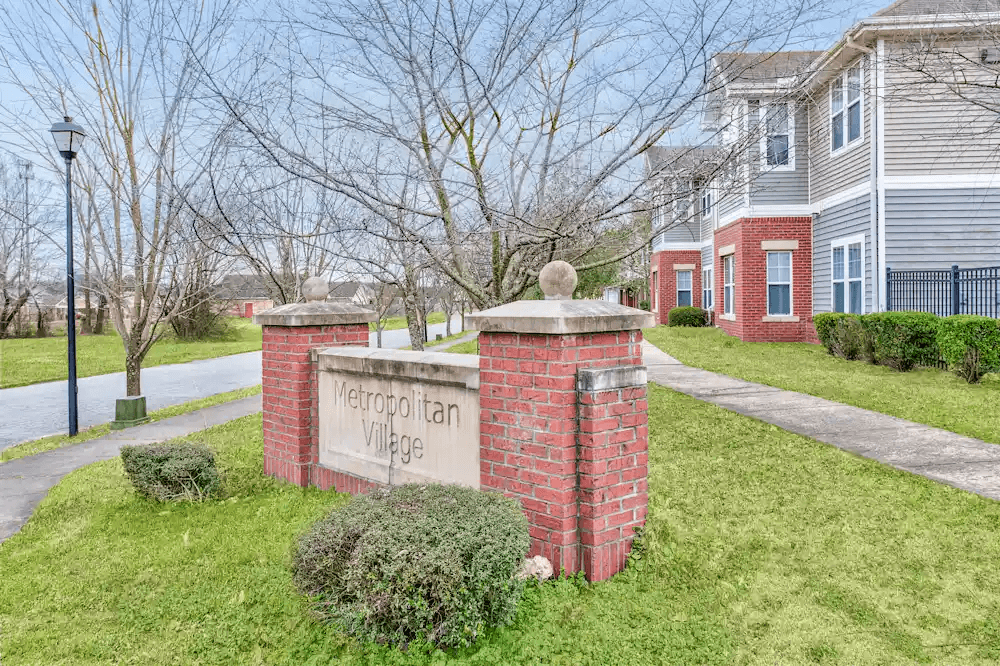 A sign that says Metropolitan Village stands in front of a brick building.
