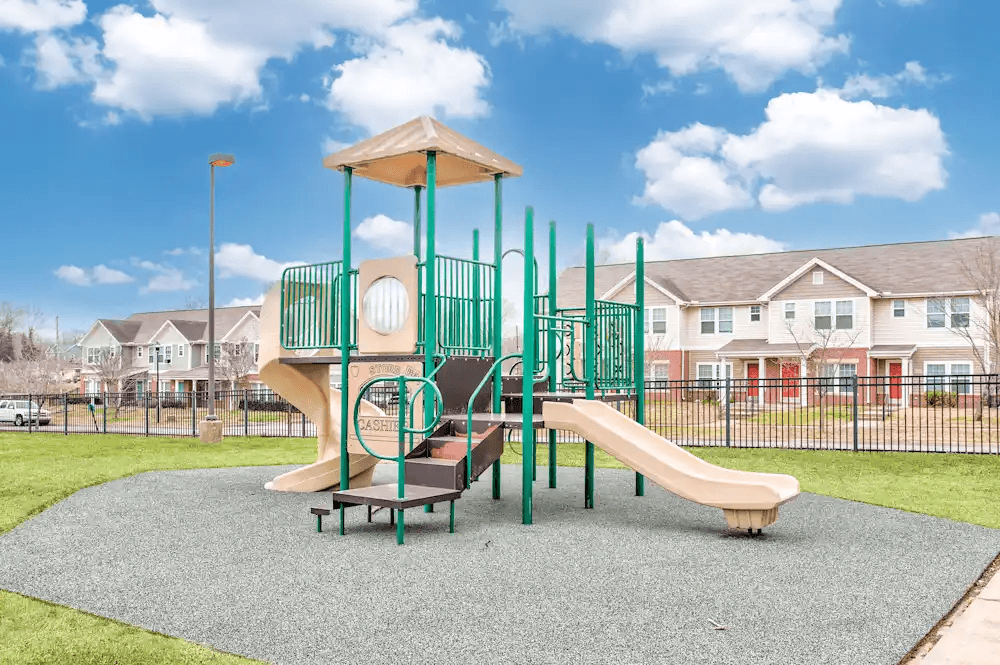 A playground with a green slide and a brown roofed structure.
