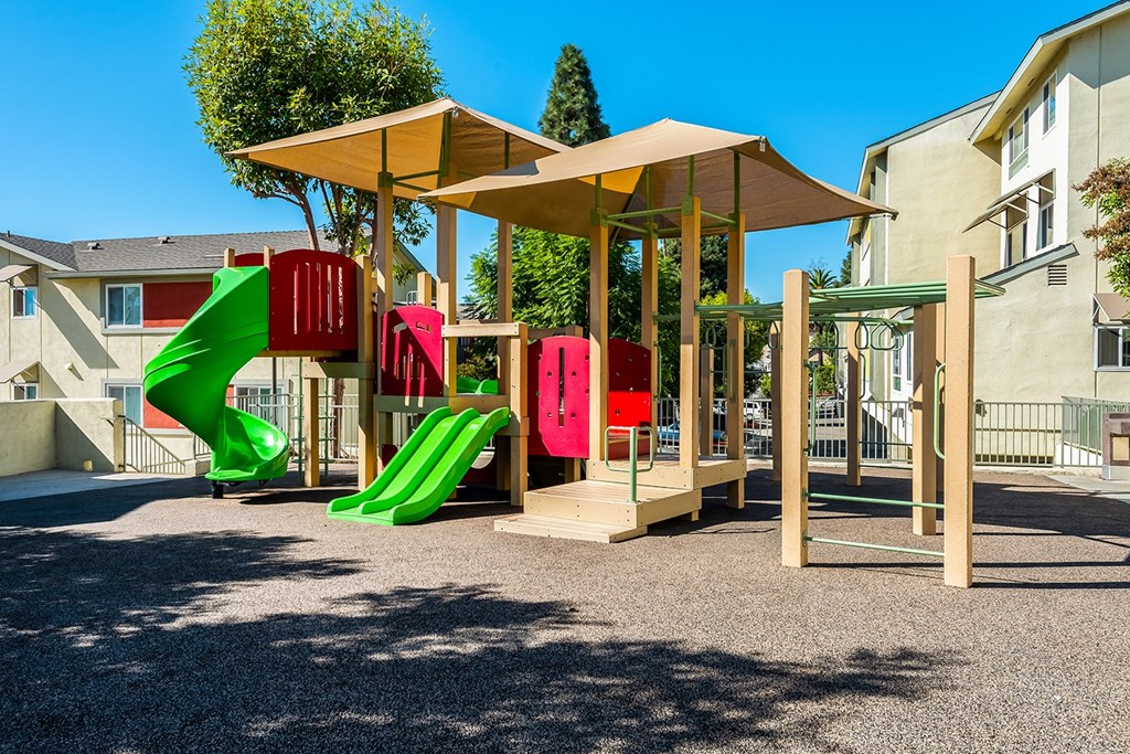 A playground with a green slide and a red and pink slide.