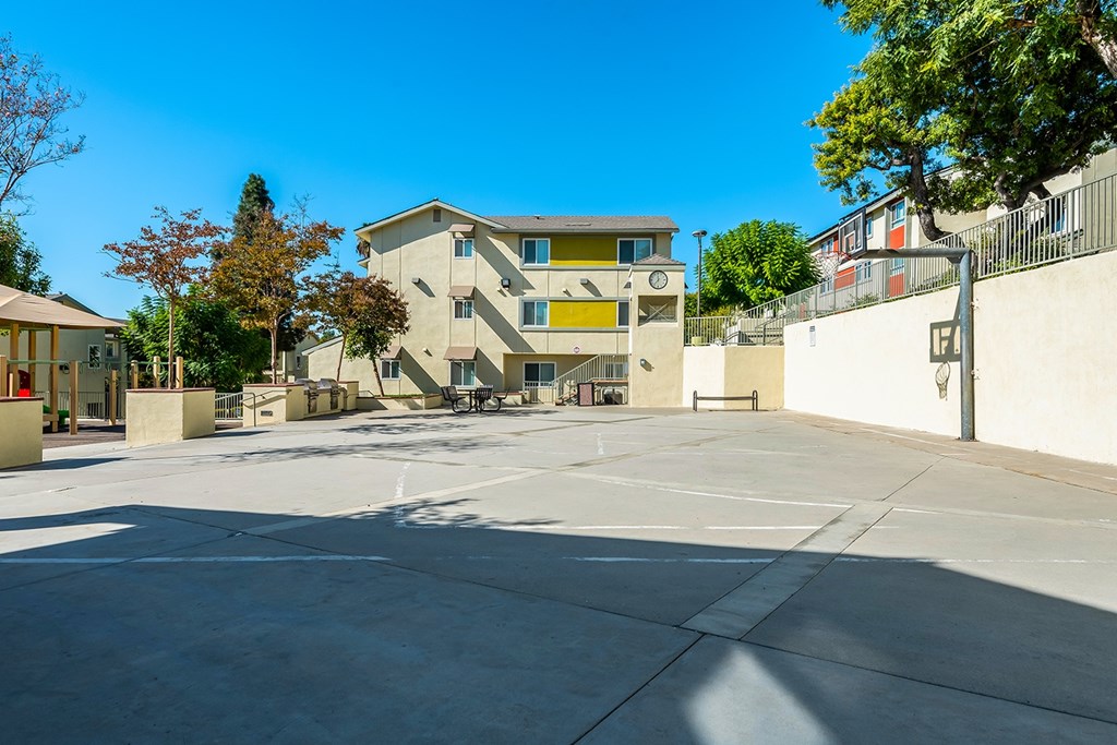 A large, open courtyard in front of a multi-story building with trees and a fence.
