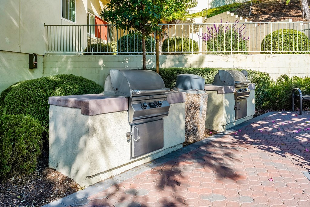 A row of outdoor grills are lined up on a brick walkway.