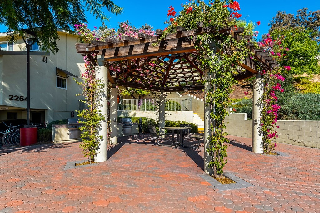 A brick patio with a pergola and flowering plants.
